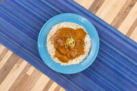 Butter Chicken Butter Chicken curry sauce with meat ladled over rice on a blue plate, topped with thin garnish strands