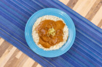 Butter Chicken Butter Chicken in orange-brown sauce over rice on a blue plate, garnished with fine shredded zest.