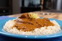 Butter Chicken Butter Chicken in a brown tomato sauce over white rice on a blue plate, garnished with citrus zest.