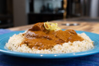 Butter Chicken Blue plate of Butter Chicken in tomato gravy over herbed rice, topped with citrus zest.