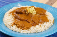 Butter Chicken Butter Chicken pieces in tomato sauce over herbed rice on a blue plate, garnished with julienned zest.