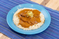 Butter Chicken Butter Chicken pieces in orange-brown sauce over rice on a blue plate, garnished with shredded strands
