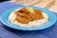 Butter Chicken Butter Chicken chunks in thick brown sauce over rice, topped with yellow garnish strands, on a turquoise plate