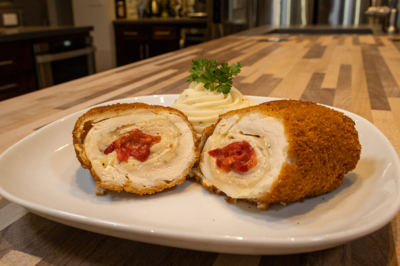 Chicken Cordon Bleu Sliced Chicken Cordon Bleu with red pimento filling, served with piped mashed potatoes and parsley on a white plate.