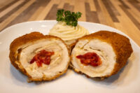 Chicken Cordon Bleu Sliced Chicken Cordon Bleu showing melted cheese and pimento pepper filling, plated with piped mashed potato.