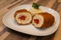 Chicken Cordon Bleu Sliced Chicken Cordon Bleu on a white plate showing cheese and pimento filling, with piped mashed potato and parsley.