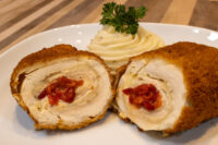 Chicken Cordon Bleu Sliced Chicken Cordon Bleu with red pimento filling, plated with piped mashed potatoes and parsley.
