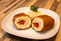 Chicken Cordon Bleu Sliced breaded Chicken Cordon Bleu roll with pimento pepper filling, plated with piped mashed potato and parsley.