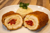 Chicken Cordon Bleu Sliced Chicken Cordon Bleu showing red pimento filling, plated with a mashed potato swirl and parsley.