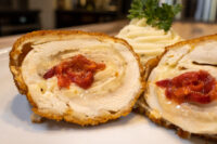 Chicken Cordon Bleu Sliced Chicken Cordon Bleu showing melted cheese and pimento pepper filling, with mashed potato and parsley behind.
