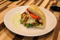 Chicken Gyros Chicken Gyros sandwich on a crusty roll with grilled chicken, tomato, onion, greens, and green sauce.