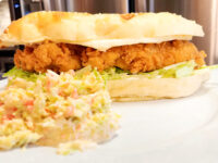 Chicken Tenders Crispy chicken tenders sandwich with melted cheese and lettuce on a toasted bun, served with coleslaw.