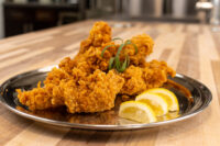Chicken Tenders Crispy Chicken Tenders piled on a metal plate with lemon wedges and a green herb garnish.