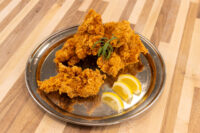 Chicken Tenders Crispy fried Chicken Tenders piled on a metal plate with lemon wedges and a green herb garnish