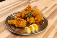 Chicken Tenders Golden crispy Chicken Tenders piled on a metal plate with lemon wedges and a herb garnish.
