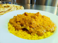 Chicken Tikka Masala Chicken Tikka Masala pieces in creamy orange sauce over yellow rice, naan bread visible behind the plate.