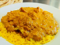 Chicken Tikka Masala Chicken Tikka Masala in creamy orange sauce spooned over yellow rice on a white plate.