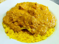Chicken Tikka Masala Chicken Tikka Masala in creamy orange sauce served over turmeric yellow rice on a white plate.