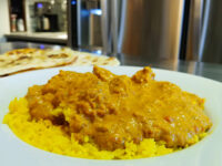 Chicken Tikka Masala Plate Chicken Tikka Masala in creamy orange sauce over yellow rice, with naan bread visible behind the plate.