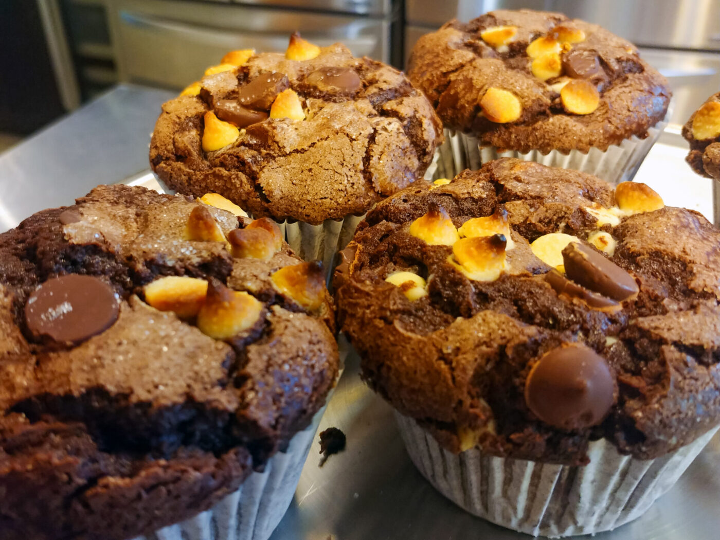 Chocolate Muffins Four Chocolate Muffins with chocolate chips and toasted marshmallow bits on a metal tray.
