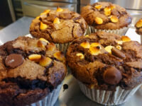 Chocolate Muffins Four Chocolate Muffins with chocolate chips and toasted marshmallow bits on a metal tray.