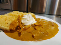 Creamy Paprika Chicken Kuře na Paprice Creamy Paprika Chicken Kuře na Paprice with sour cream on a plate beside sliced dumpling bread.