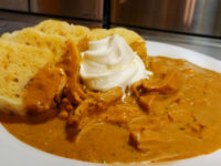 Kuře na Paprice Plated Plate of Creamy Paprika Chicken Kuře na Paprice with shredded chicken in paprika sauce, whipped cream, and bread dumplings.