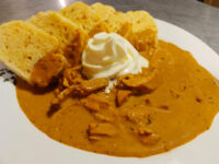 Creamy Paprika Chicken Kuře na Paprice Bowl of Creamy Paprika Chicken Kuře na Paprice with shredded chicken, sour cream dollop, and toasted bread slices.