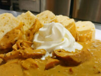Creamy Paprika Chicken Kuře na Paprice Bowl of Creamy Paprika Chicken Kuře na Paprice with a whipped cream dollop, ringed by bread slices