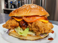 Crispy Chicken Sandwich with BBQ Sauce Crispy Chicken Sandwich with BBQ Sauce on a sesame bun with lettuce, tomato, cheese, and red sauce.