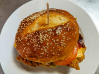 Crispy Chicken Sandwich with BBQ Sauce Crispy Chicken Sandwich with BBQ Sauce on a sesame bun with cheese and tomato, held with a skewer.