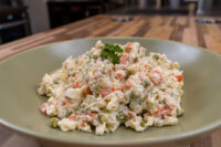 Bowl of Czech Potato Salad with diced potatoes, carrots, and peas, garnished with parsley on a green plate.