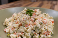 Bowl of Czech Potato Salad with diced potatoes, carrots, peas, and creamy dressing on a green plate.