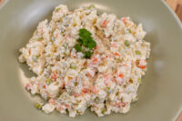 Czech Potato Salad in a creamy dressing with diced carrots and peas, garnished with parsley, on a green plate.