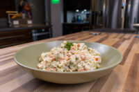 Bowl of Czech Potato Salad with creamy dressing, diced carrots, peas, and herb garnish on a wooden table.