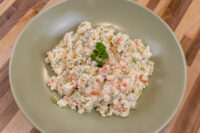 Bowl of Czech Potato Salad with peas, diced carrot, and potato, garnished with parsley.