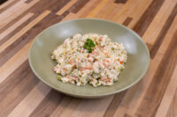 Bowl of Czech Potato Salad with peas, diced carrots, and creamy dressing, topped with parsley.