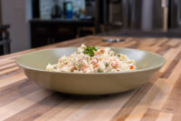 Bowl of Czech Potato Salad with diced carrot and pea pieces, garnished with parsley, on a wood table.