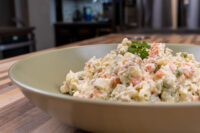 Large bowl of Czech Potato Salad with diced potatoes, carrots, peas, and parsley on a wooden table.