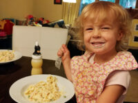 Fettuccine Alfredo with Chicken Toddler with sauce on her face holds a fork over a plate of Fettuccine Alfredo with peas in creamy sauce.