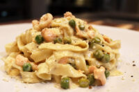 Fettuccine Alfredo with Salmon Plate of Fettuccine Alfredo with Salmon, showing creamy pasta, peas, and flaked salmon under grated cheese and pepper.
