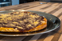 Frgal Kolach with Plum Filling on a metal plate, streusel scattered over dark plum filling, set on a wooden table.