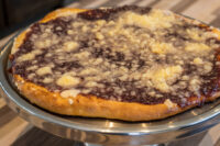 Round Frgal Kolach with Plum Filling, dark filling and streusel topping, on a metal cake stand.
