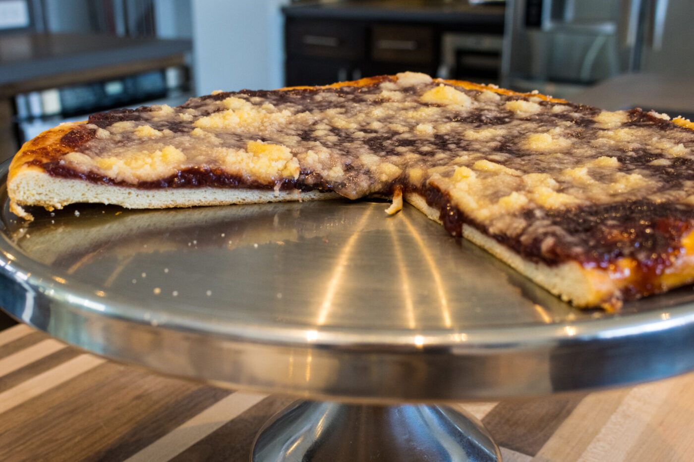 Square Frgal Kolach with Plum Filling, streusel-topped, with a cut slice showing the dark filling on a metal stand.