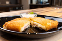 Fried Cheese with Ham Fried Cheese with Ham cut in half showing melted cheese and ham, on a black plate with a creamy dip.