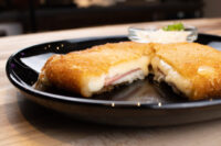 Fried Cheese with Ham Fried Cheese with Ham sliced open on a black plate, showing melted cheese and ham, with a dip alongside.