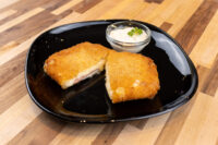 Fried Cheese with Ham Halved Fried Cheese with Ham on a black plate, showing melted cheese and ham, with a dip alongside