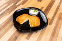 Fried Cheese with Ham Two breaded, fried halves of Fried Cheese with Ham on a black plate, with a creamy dip and herb garnish.