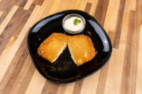Fried Cheese with Ham Two halves of Fried Cheese with Ham, breaded and golden, on a black plate with a creamy herb-topped dip.