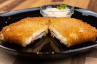 Fried Cheese with Ham Halved Fried Cheese with Ham showing melted cheese and ham inside crispy breading, with dip on black plate